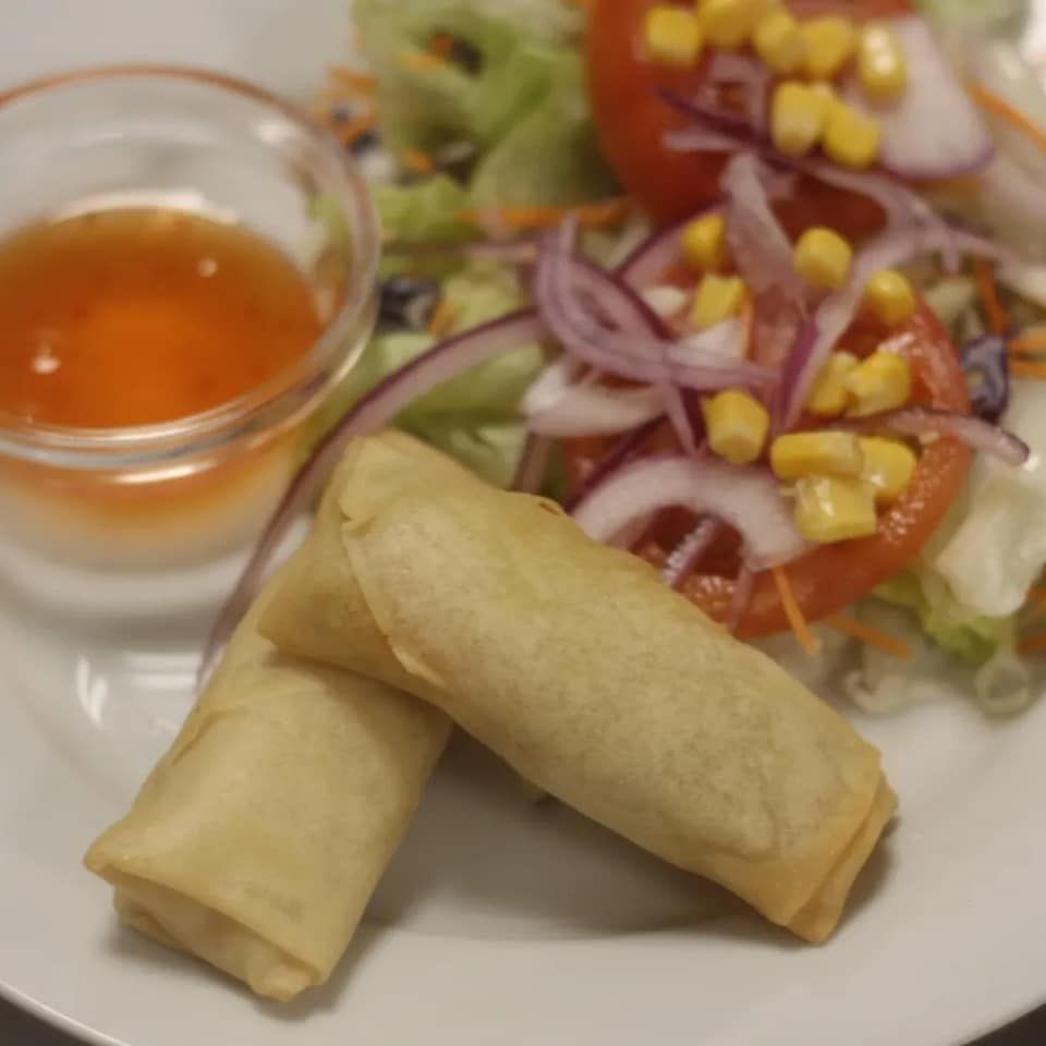 Un plato blanco cubierto con rollitos de primavera y ensalada.