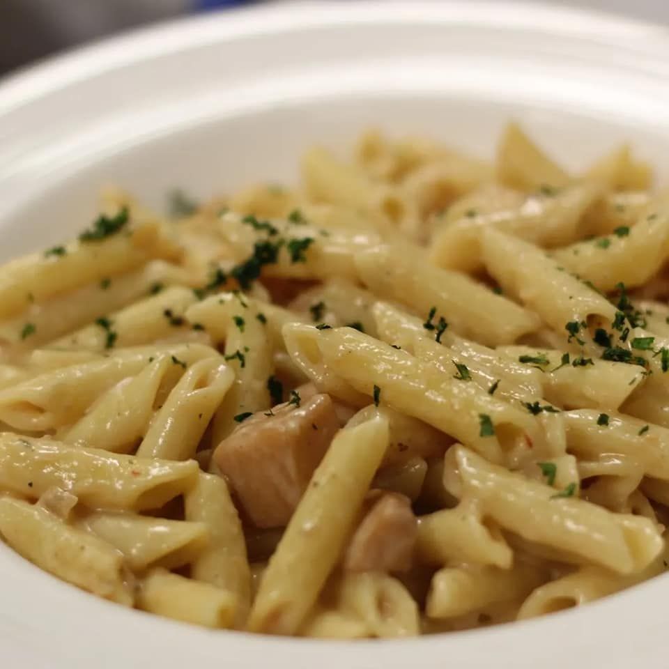 Un plato de pasta con pollo y perejil encima.