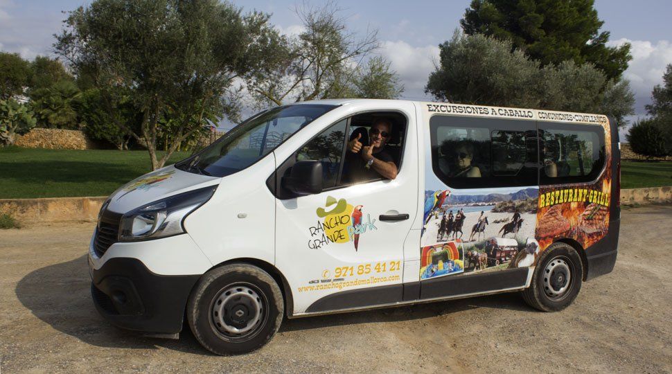 Una camioneta blanca está estacionada en un lote de tierra con árboles al fondo.