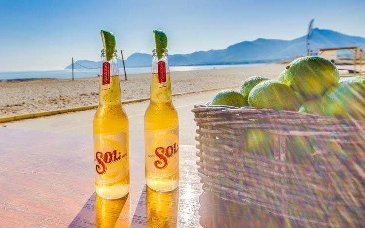 Dos botellas de cerveza sol están sobre una mesa al lado de una cesta de limas.