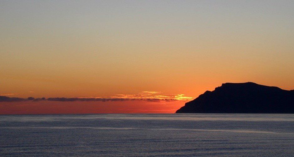 Una puesta de sol sobre el océano con una montaña a lo lejos