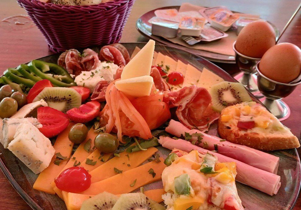 Un plato de comida con jamón, queso, verduras y huevos en una mesa.