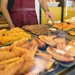 Un hombre está de pie detrás de una vitrina llena de una variedad de pasteles.