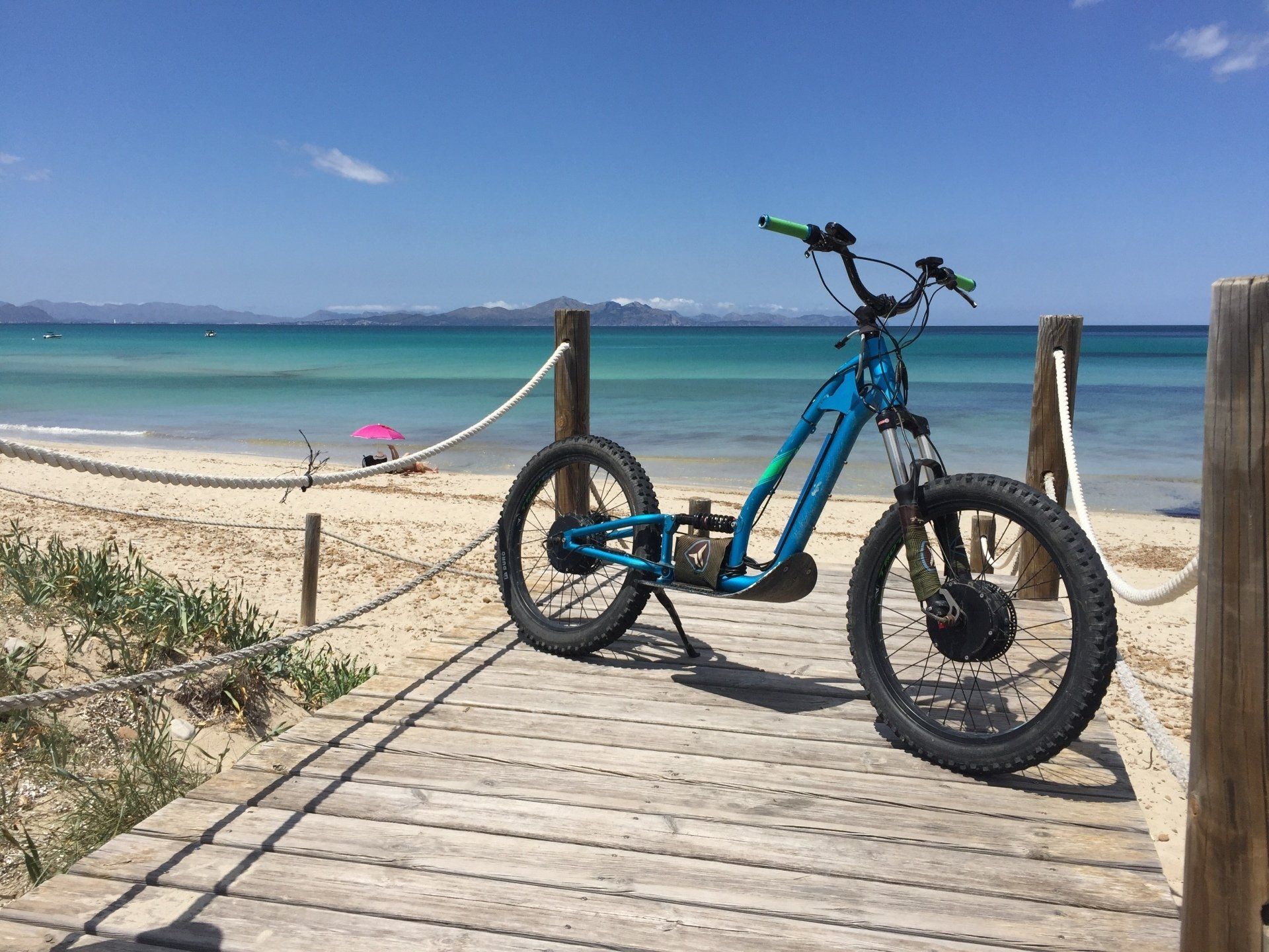 Una scooter azul está estacionada en una pasarela de madera al lado de la playa.