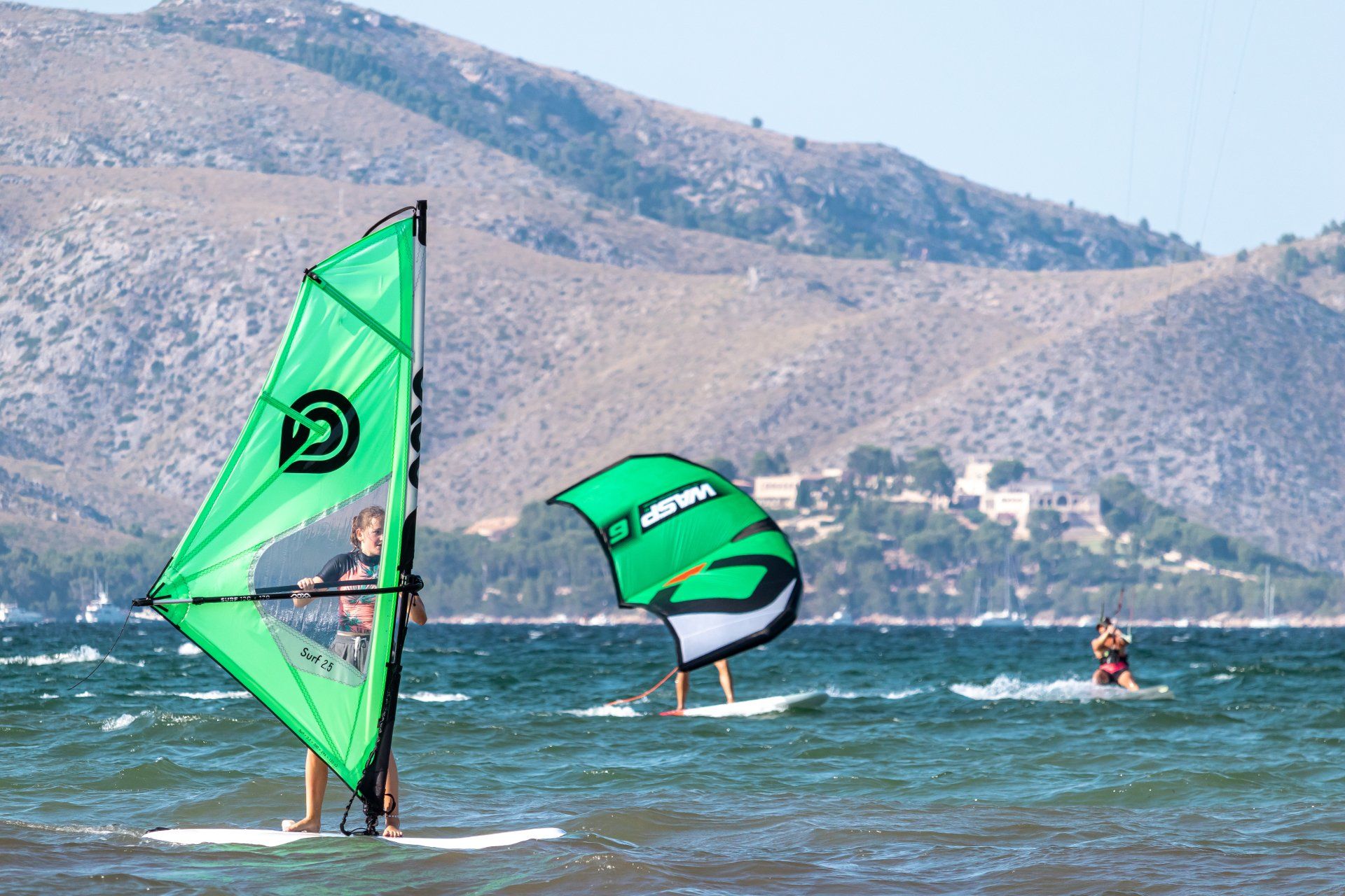 Dos personas hacen windsurf en el océano con montañas al fondo.