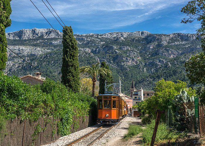 Un tren va bajando por unas vías con montañas al fondo.