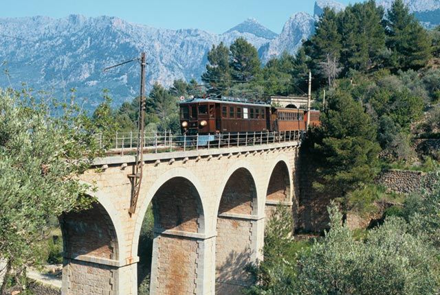 Un tren pasa por un puente con montañas al fondo.