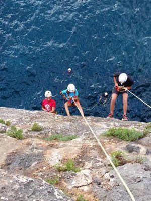 Un grupo de personas está escalando una pared de roca cerca del océano.