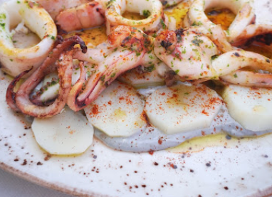 Un plato de comida con calamares, camarones y patatas en una mesa.