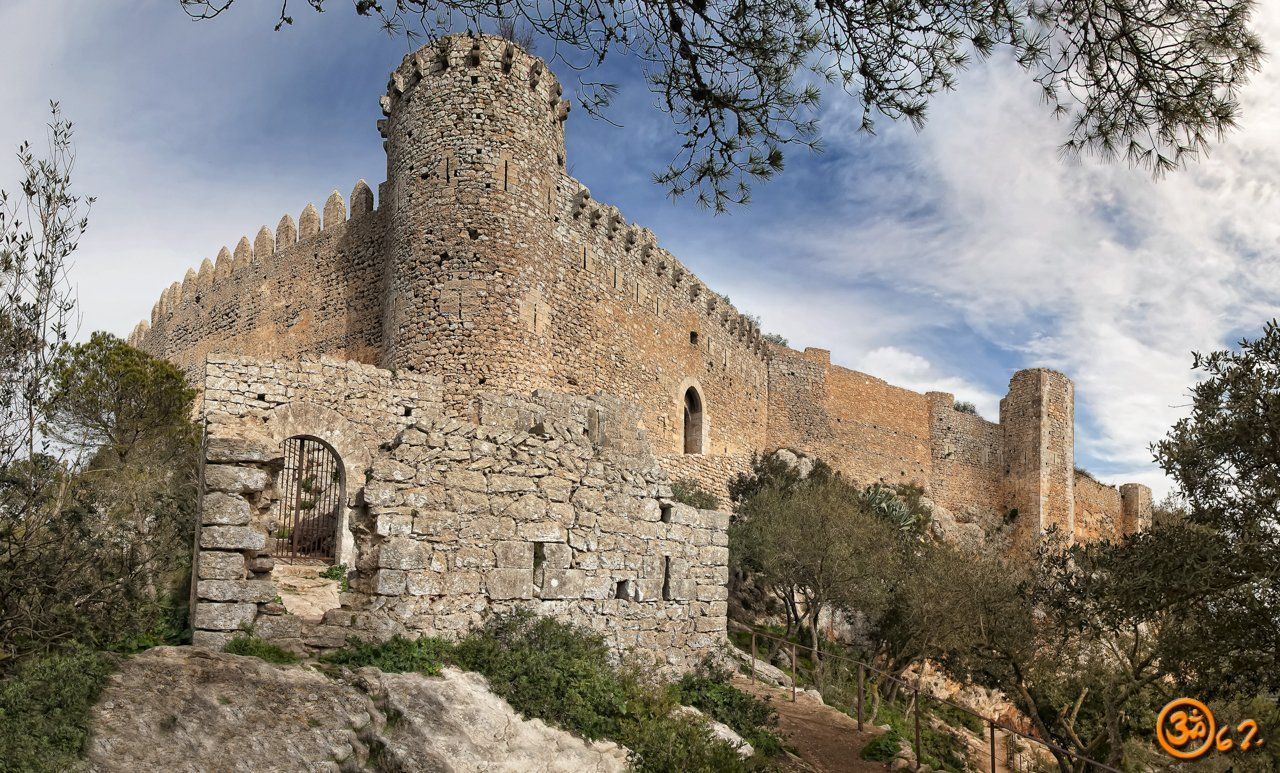 Un gran castillo de piedra se encuentra en la cima de una colina rodeado de árboles.