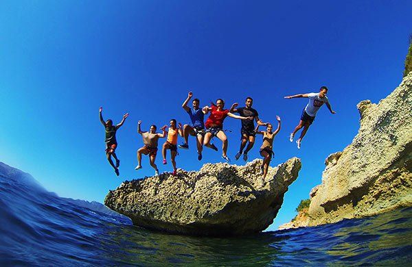 Un grupo de personas salta desde una roca al océano.