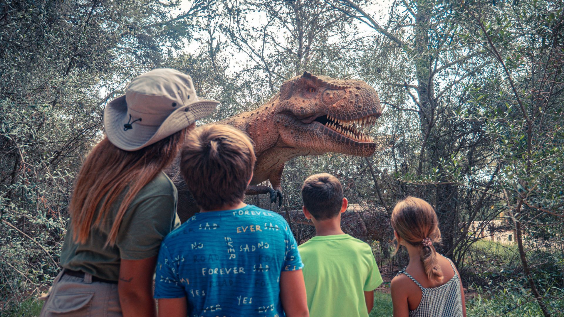 Un grupo de niños está mirando un dinosaurio en el bosque.