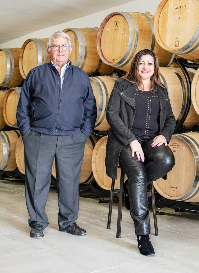 Un hombre y una mujer están parados uno al lado del otro frente a una fila de barriles de vino.