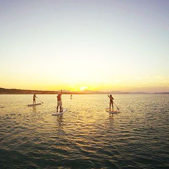 Un grupo de personas están montando tablas de remo en el océano al atardecer.