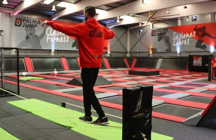 Un hombre con una chaqueta roja se balancea sobre una cuerda en un parque de trampolines.