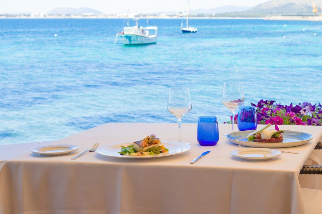 Una mesa con platos de comida y copas de vino con vista al océano.