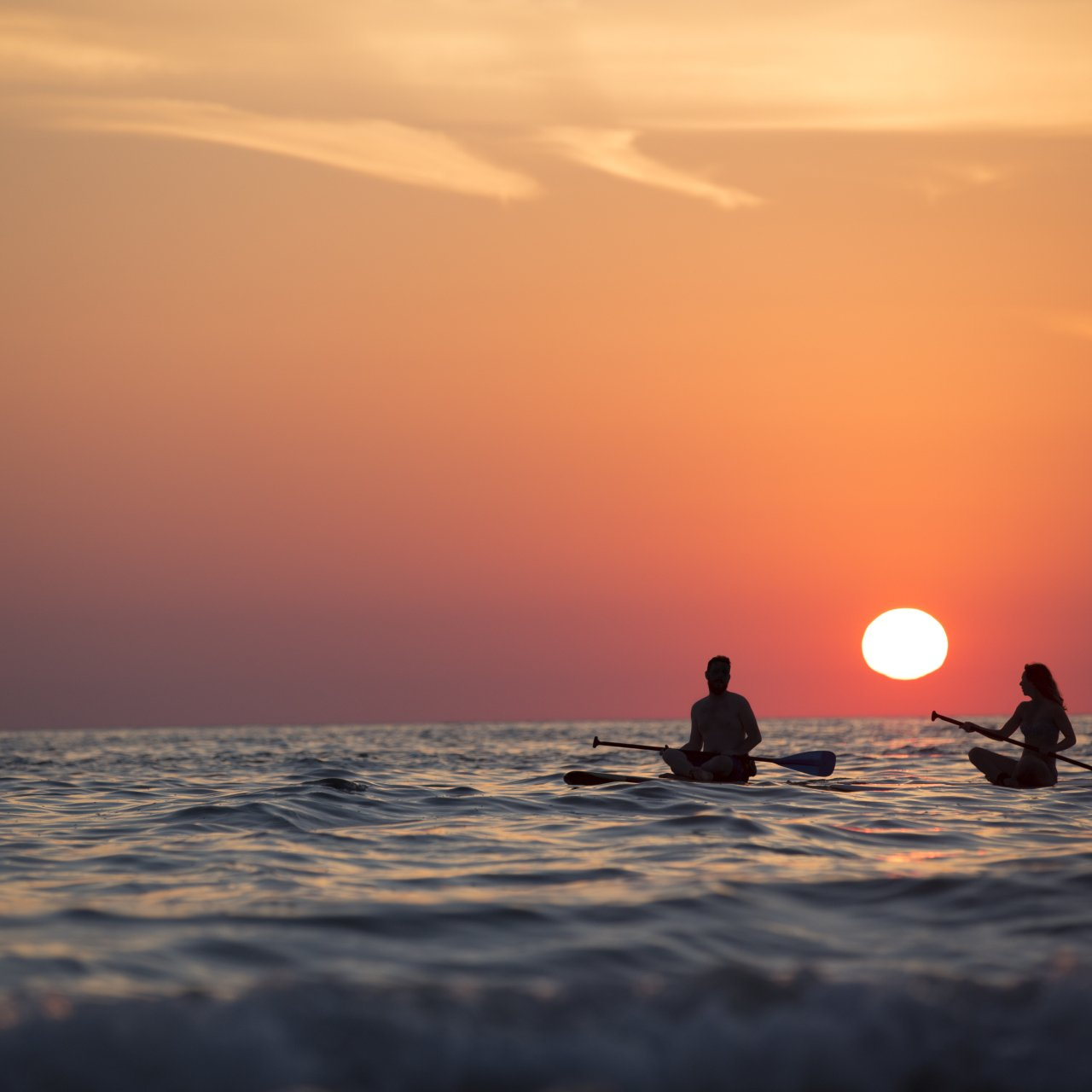 Dos personas en kayaks en el océano al atardecer.