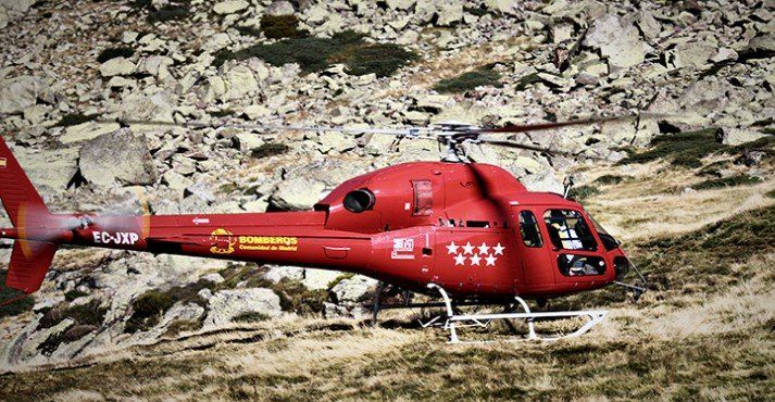 Un helicóptero rojo está volando sobre una ladera rocosa.