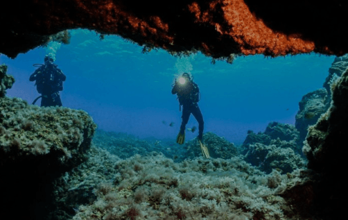 Dos buceadores están nadando en una cueva en el océano.