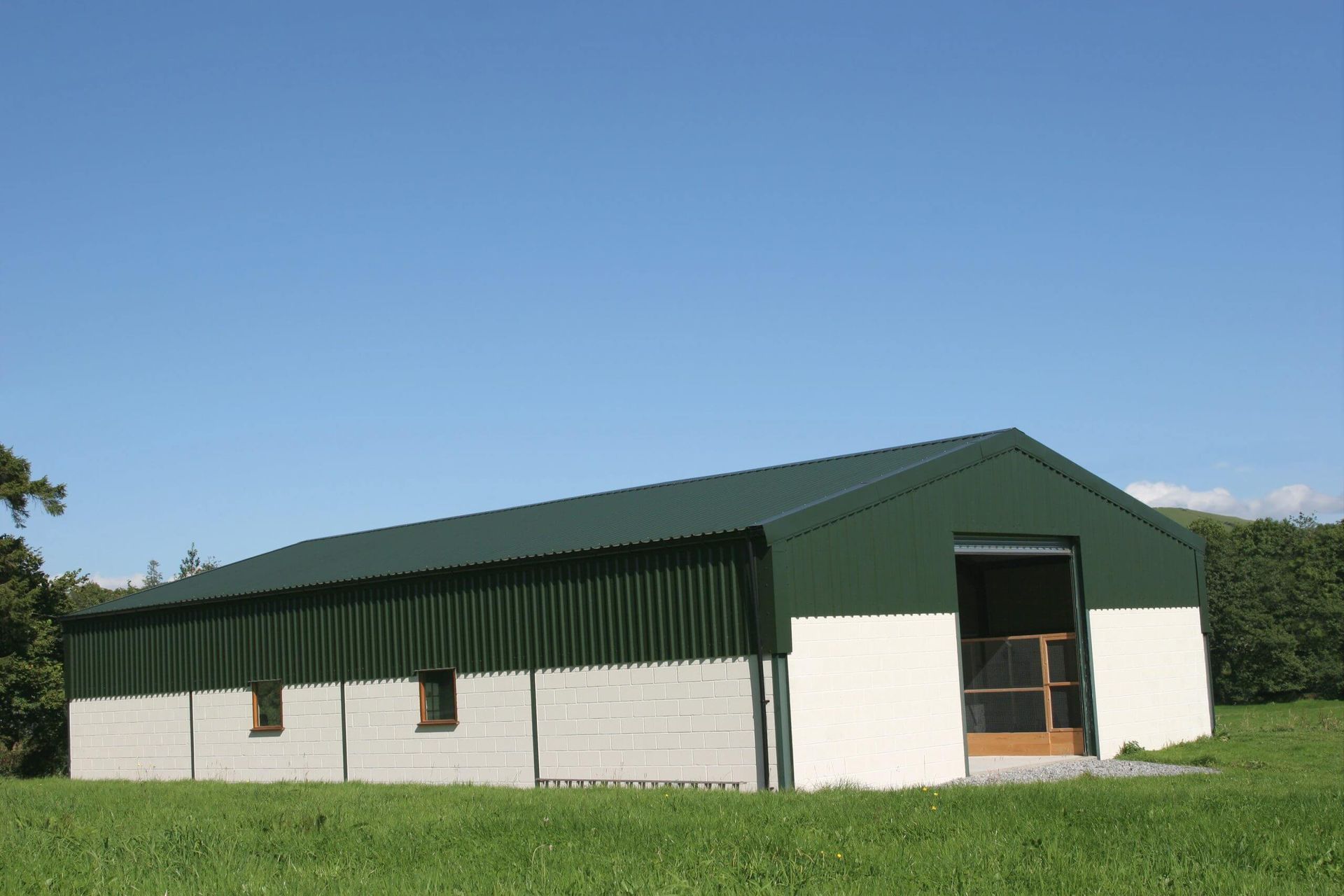 A green and white building is sitting in the middle of a grassy field.