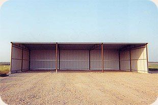 A large metal building is sitting in the middle of a dirt field.