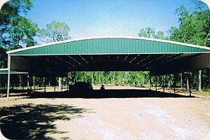 A car is parked under a green roof in a parking lot.