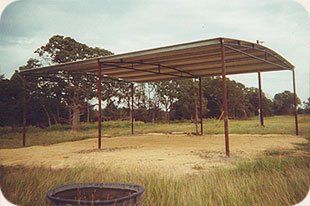 A carport in the middle of a field with trees in the background.