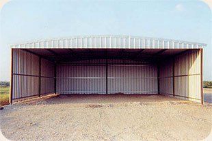 A large metal building with a clear roof is sitting on top of a dirt field.