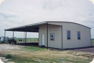 A large metal building with a canopy over it is sitting in the middle of a field.