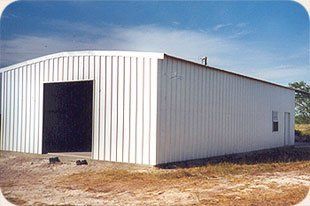 A large white metal building is sitting in the middle of a dirt field.