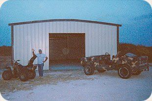 A man is standing next to a jeep and a motorcycle in front of a garage.