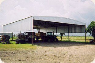 A tractor is parked under a shed in a field.