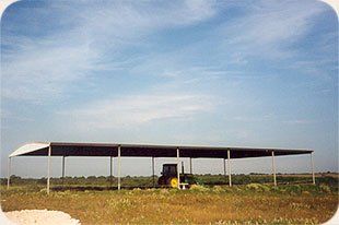 A tractor is parked under a canopy in a field.