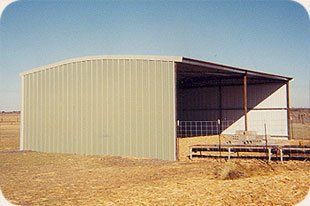 A large metal building is sitting in the middle of a field.