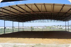 A large metal structure with a roof over a dirt field.