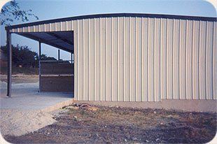 A white metal building with a black roof is sitting in the middle of a dirt field.