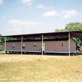 A mobile home with a covered roof is sitting in the middle of a grassy field.
