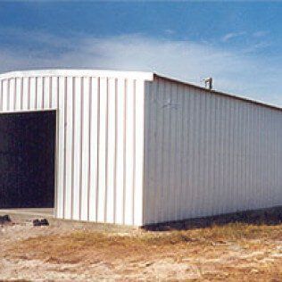 A white metal building is sitting in the middle of a field.