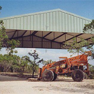 An orange tractor is parked under a green roof.