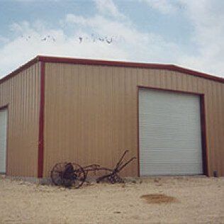 A metal building with a garage door and a wheelbarrow in front of it.