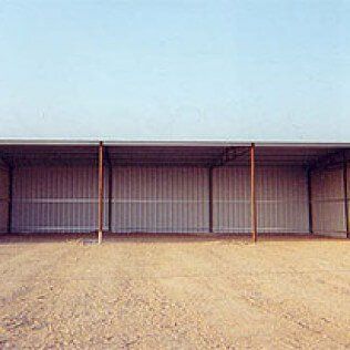 A row of sheds in a dirt field with a blue sky in the background.