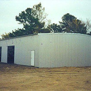 A large white metal building is sitting in the middle of a dirt field.
