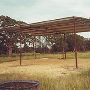 There is a covered area in the middle of a field with trees in the background.