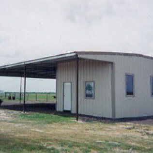 A metal building with a canopy over it is in the middle of a field.