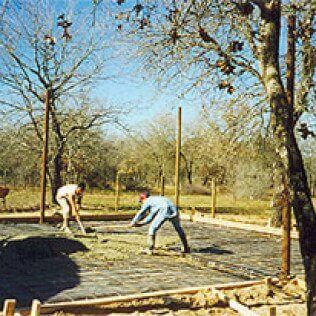 Two men are working on a concrete base in a field.