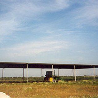 A tractor is parked under a canopy in a field.