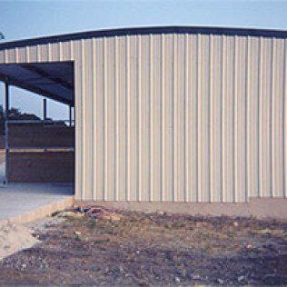 A white metal building with a black roof is sitting on top of a dirt field.