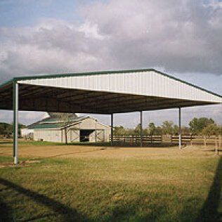 There is a covered area in the middle of a field with a barn in the background.