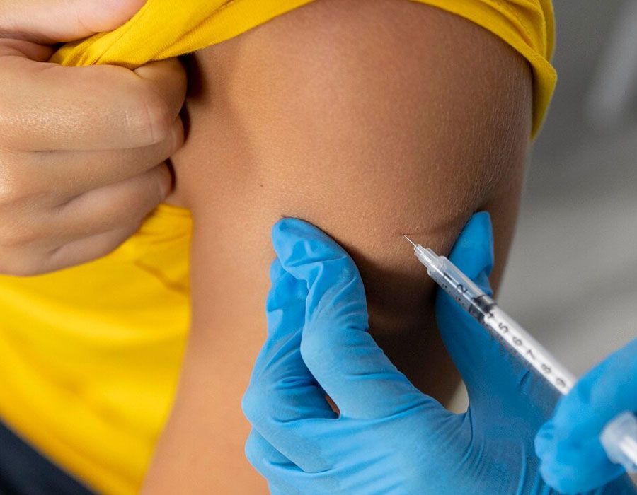 Gloved hands giving a syringe injection into an arm with a yellow sleeve