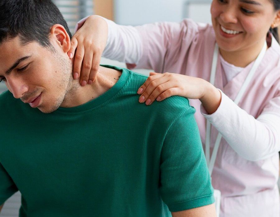 A woman massages a seated man’s neck and shoulders as he leans forward in a green shirt.
